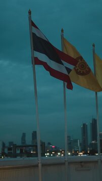 Thai and buddhist flags waving in the wind against the bangkok city skyline in the evening
