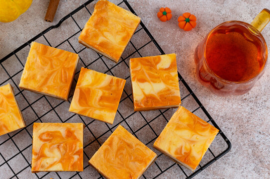 Pumpkin marble cheesecake bars on a metal rack with mini pumpkin decor and tea, styled in autumn tones. Cozy fall dessert perfect for Thanksgiving or Halloween. Top view.