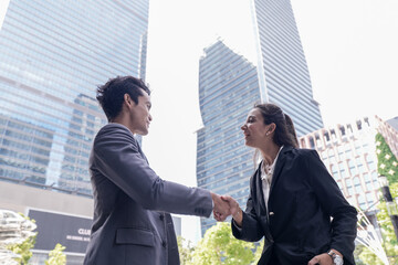 A diverse pair of business professionals greeting each other with a handshake at the foot of a glass skyscraper, showing how business happens beyond the meeting room © ultramansk