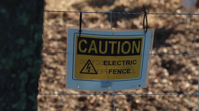 Electric fence caution warning sign hanging on wire fence indicates an electric shock hazard and warns people about danger around the fenced area