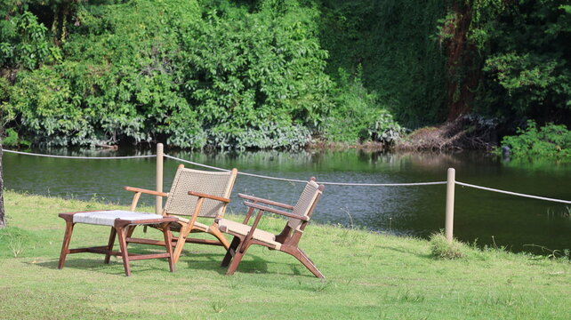 The image depicts three outdoor chairs arranged on a well maintained grassy area near a body of water, likely a river or lake