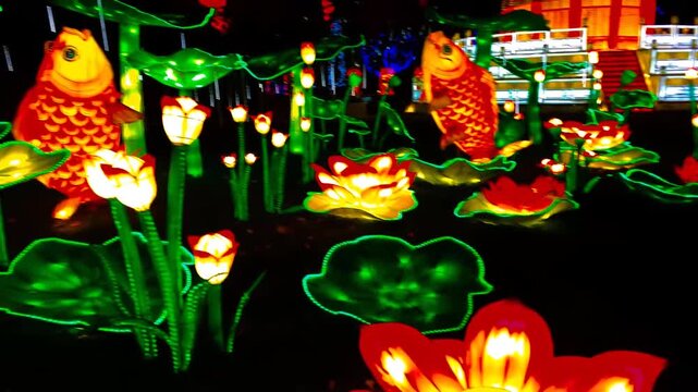 Illuminated lotus and koi fish lanterns glow in a nighttime garden display with glowing lily pads and floral motifs