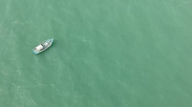 Aerial top-down view of a solitary blue fishing boat drifting on calm turquoise sea waters