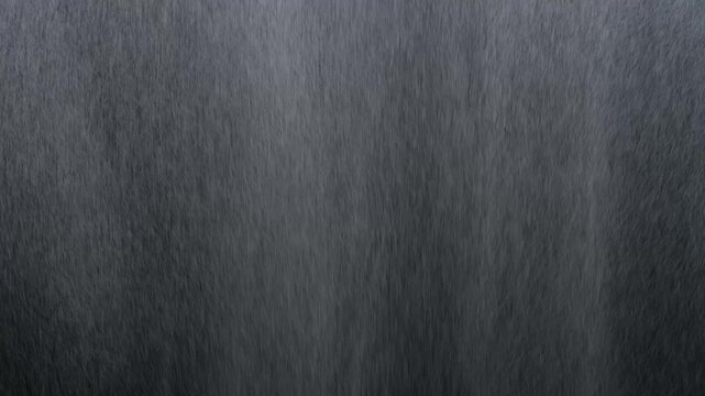 Heavy rain falling on dark metallic surface with visible water streaks and runoff patterns