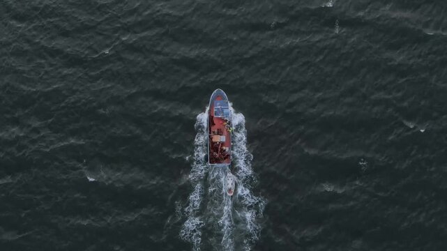 Aerial drone view of a fishing boat navigating choppy open sea with a smaller support vessel trailing behind