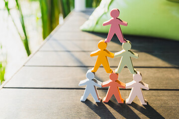 Leadership and teamwork hierarchy concept, colorful human figures stacked in pyramid on wooden deck...