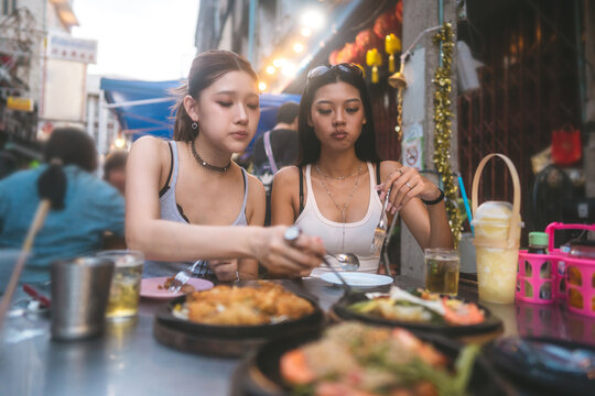  Two young asian adult women Gen Z foodie eating Thailand street food travel in Bangkok city at chinatown Yaowarat