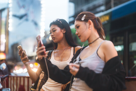 Two young asian women using smart phone wear gen Z street fashion style outfit travel in Bangkok