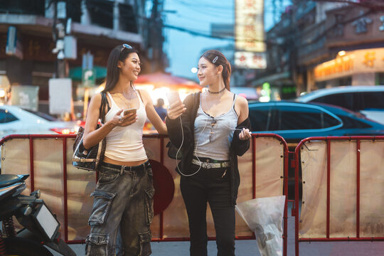 Two young asian women using smart phone wear gen Z street fashion style outfit travel in Bangkok