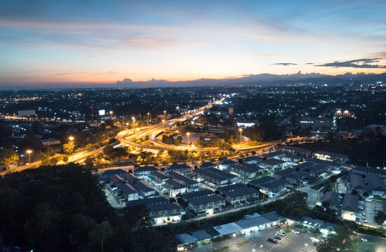Aerial cityscape at blue hour over Don Chan intersection in Chiang Mai, Thailand, showing illuminated highway traffic, urban road and glowing neighborhoods for travel, transport and infrastructure use