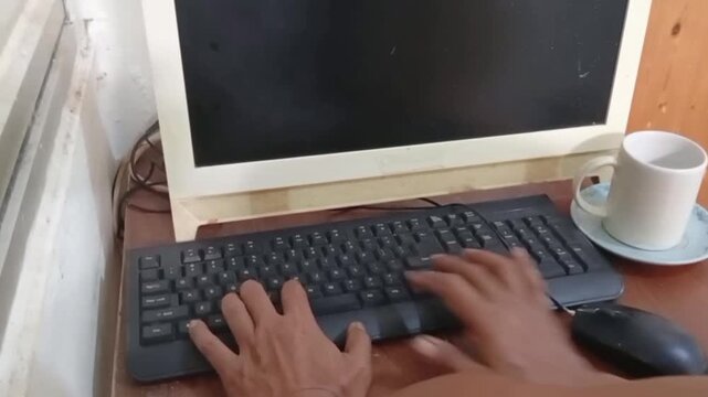 Close up of male hands typing on keyboard and drinking coffee while working on computer.