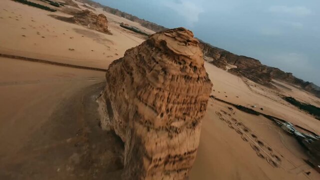 Aerial drone flyover of the iconic Elephant Rock formation in AlUla, Saudi Arabia, showcasing layered sandstone cliffs and desert terrain under soft twilight light