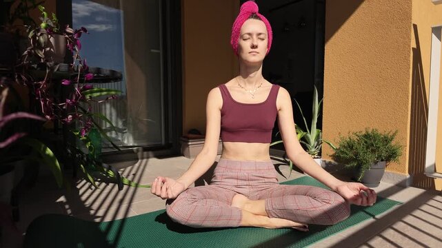 Woman sitting in a cross-legged meditation pose on a yoga mat outdoors. She maintains a calm posture with her hands resting on her knees while practicing mindfulness in warm sunlight
