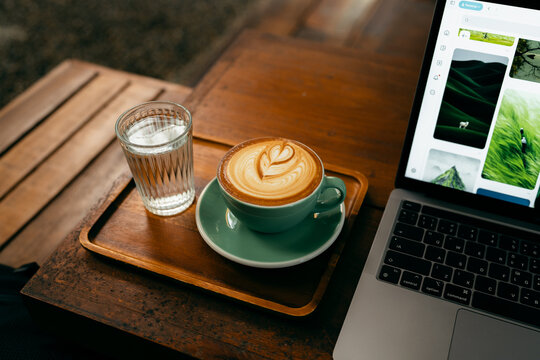 Remote work lifestyle, laptop screen showing photos with a cup of hot coffee on rustic wooden table.
