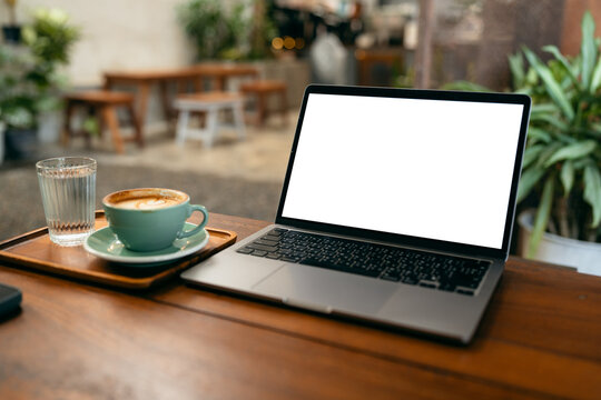 Laptop computer with blank white screen mockup on wooden table in a coffee shop with a cup of latte.