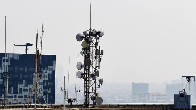 High telecommunication tower stands tall against a muted sky. Metal lattice holds many satellite dishes and antennas.
