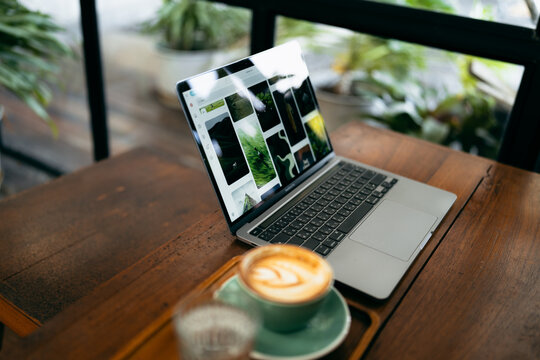 Remote work lifestyle, laptop screen showing photos with a cup of hot coffee on rustic wooden table.