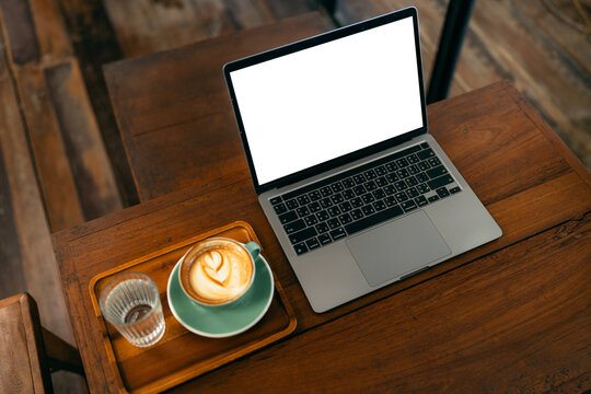 Laptop computer with blank white screen mockup on wooden table in a coffee shop with a cup of latte.