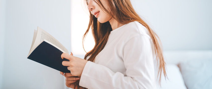 Young adult asian woman reading a book in bedroom living at home apartment satisfaction lifestyle