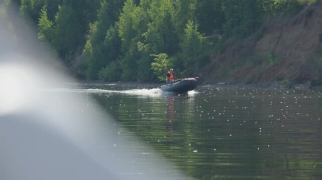 Angler steers the boat on the river as seen from another vessel