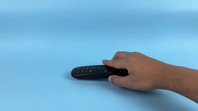 Hand Holding TV Remote Control Pointing Forward on Blue Background