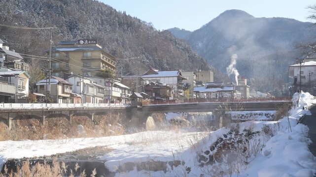 湯けむりが立ち上る雪景色の渋温泉街と横湯川の全景