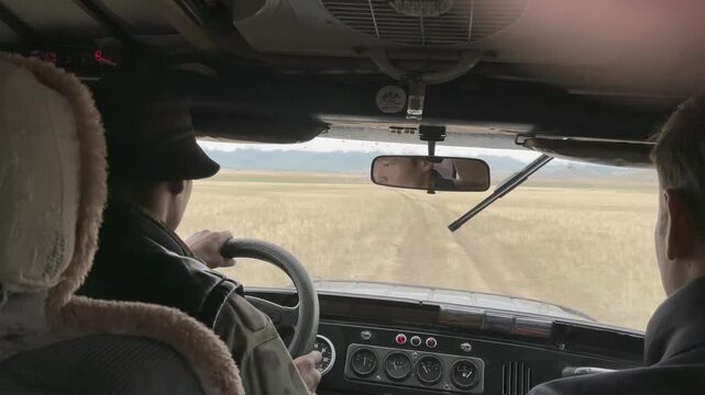 Point of view from inside a vehicle driving on a dirt track through the wide Kurai Steppe, Altai Republic, Russia, with distant mountains and cloudy sky