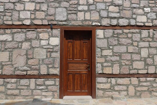 A stone wall with a brown wooden door in the center. A detail from traditional Asian architecture.