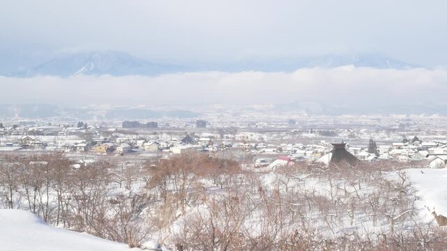 雪に覆われた町並みと雲海に浮かぶ冬の山々の壮大な俯瞰映像