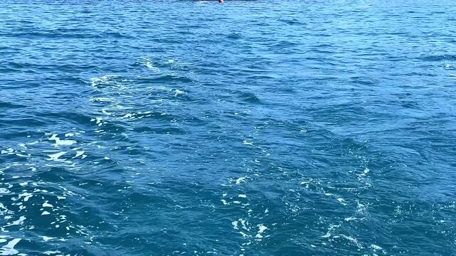 A wide water-level perspective of deep blue Aegean sea waves looking towards the white hillside villas and coastline of Bitez, Bodrum, Turkey.