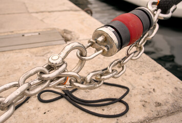 Obraz premium Heavy-duty rubber mooring shock absorber and steel chain on a stone pier in Rijeka port, Croatia. Marine yachting hardware detail.