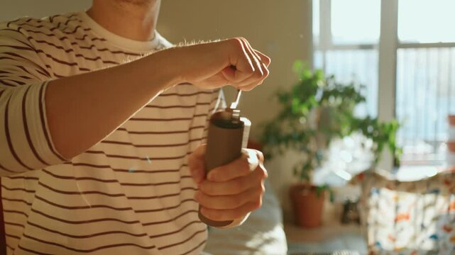 Daily morning ritual of a man grinding fresh coffee beans using a manual coffee grinder in a sunlit kitchen, enjoying the process of preparing a fresh and aromatic specialty beverage