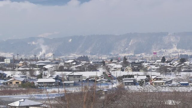 雪に覆われた冬の集落を走り抜ける長野電鉄の特急ゆけむり（1000形）