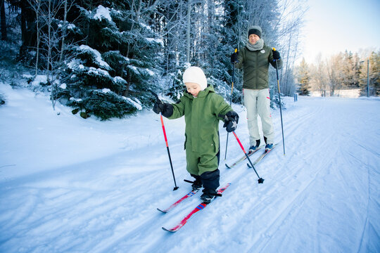 A father helps his toddler learn cross-country skiing on a snowy trail in Helsinki region, Finland, during an active winter family outing.