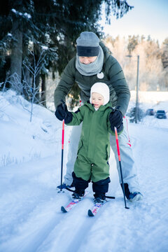 A father helps his toddler learn cross-country skiing on a snowy trail in Helsinki region, Finland, during an active winter family outing.