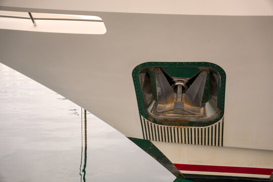 Metallic anchor mounted in the bow pocket of a white motor yacht in Rijeka harbor, Croatia. Nautical vessel design detail.