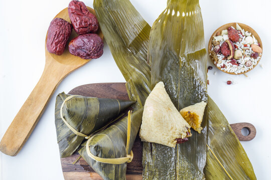 Unwrapped and wrapped zongzi with bamboo leaves, red dates, and mixed rice ingredients displayed on a wooden board.