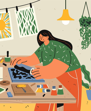 Linocut block printing drawing creative hobby artist working with ink roller on table surrounded by art supplies plants drying prints home studio