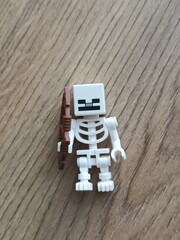 Fototapeta premium A white Lego Minecraft skeleton minifigure holding a brown plastic bow on a wooden surface