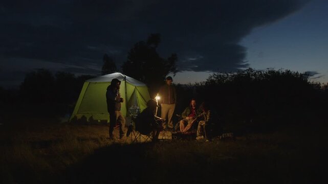 Group of men camping in the wild and gather near the bonfire and talk with each other. Fishermen camping and talk stories at night