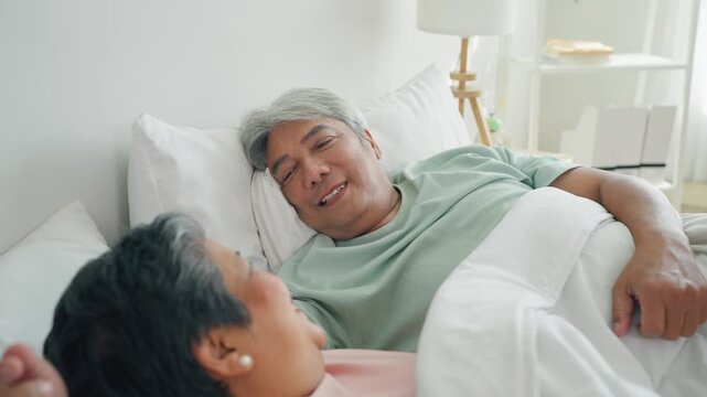Asian senior elderly couple lying down on bed and talking to each other. 