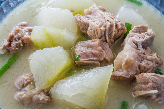 A bowl of simmered pork ribs and winter melon soup with light savory broth and green onion garnish.