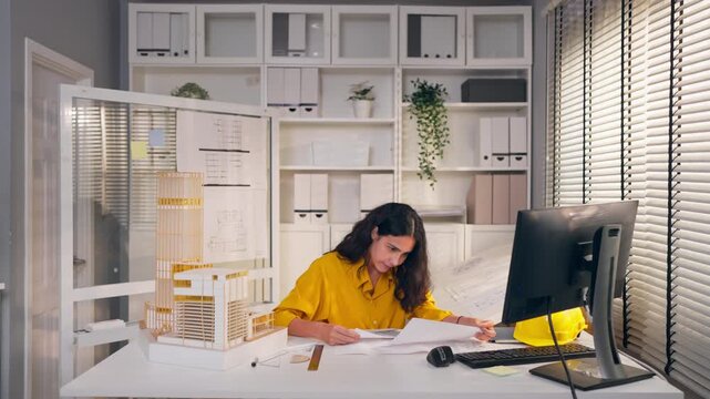 Young Hispanic woman architect sitting at desk, working in an office.