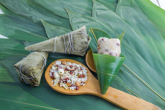 Traditional zongzi made of glutinous rice and mixed ingredients, wrapped in bamboo leaves, with raw ingredients on a wooden spoon.