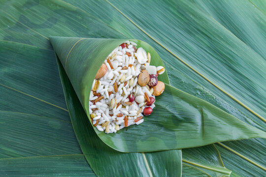 Raw mixed glutinous rice and grains placed in a folded bamboo leaf, prepared for making traditional zongzi.