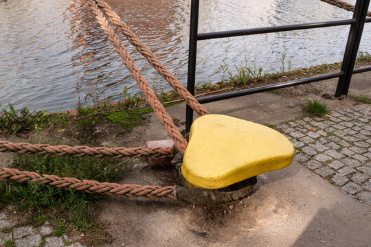 Close up of a heavy duty yellow steel mooring bollard with thick braided ropes on a harbor dock pier, maritime port infrastructure and shipping logistics concept