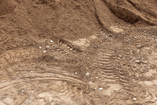 Construction site sand and soil with deep tire tracks and scattered stones, showing excavation, heavy equipment activity and rough earthy texture suitable for backgrounds, landscaping and industrial 