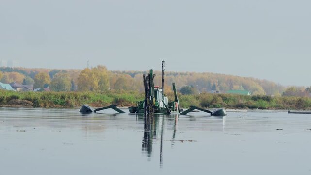Modern dredger floating excavator cleans bottom of river from silt sediments and vegetation. Drainage machine works at autumn riverside