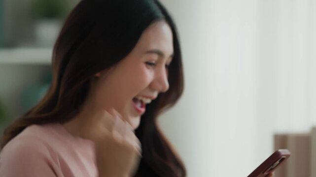 Asian woman excited on smartphone at home