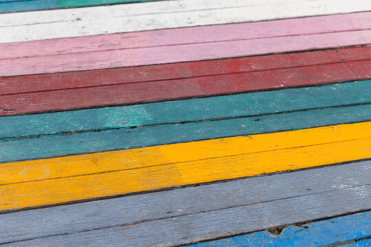Bright, weathered wooden planks painted in horizontal multicolor stripes create a rustic, textured background. Faded paint, distressed boards and vibrant hues evoke seaside charm, crafts, retro design
